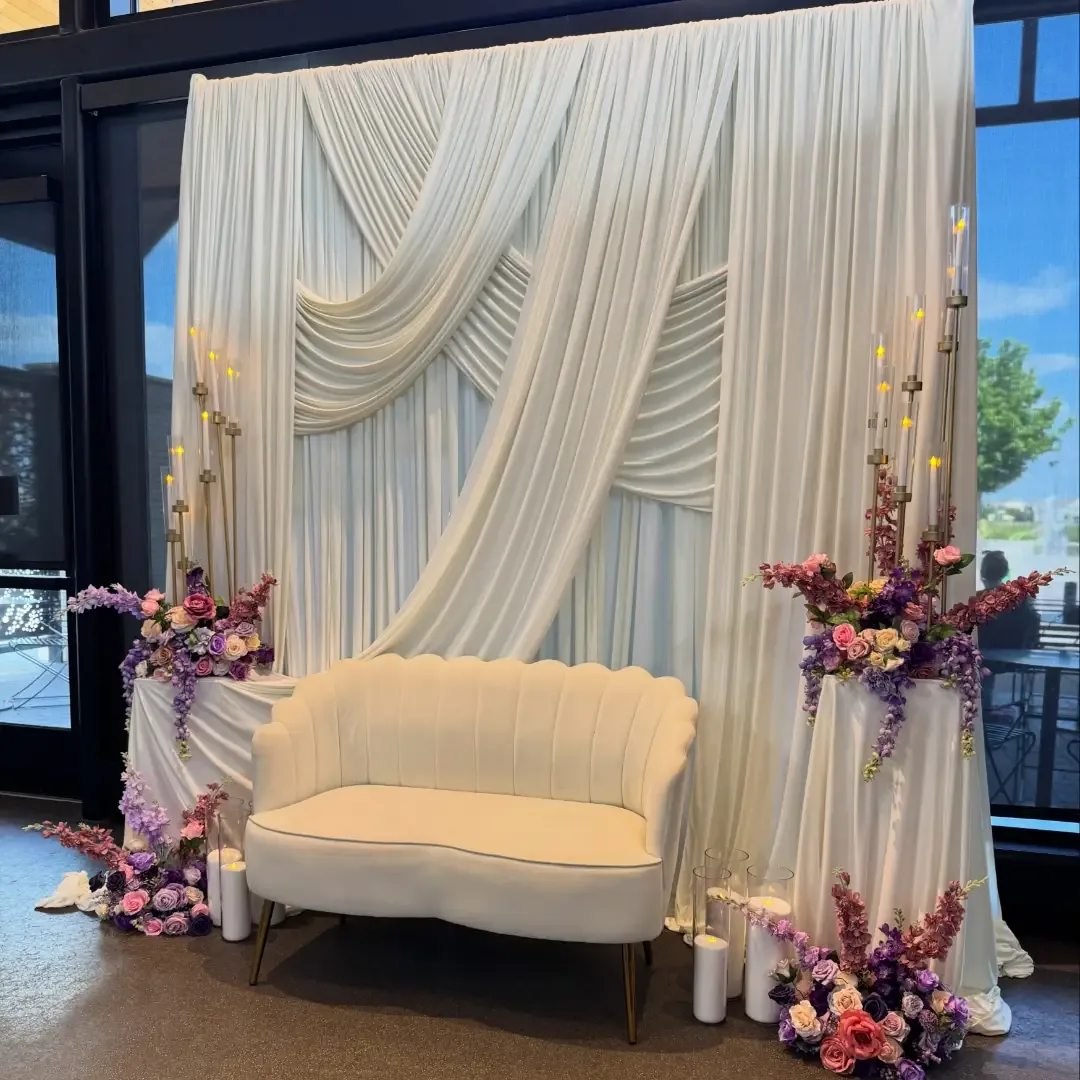 White draped backdrop with shell loveseat and pink purple florals by Smartest Decor