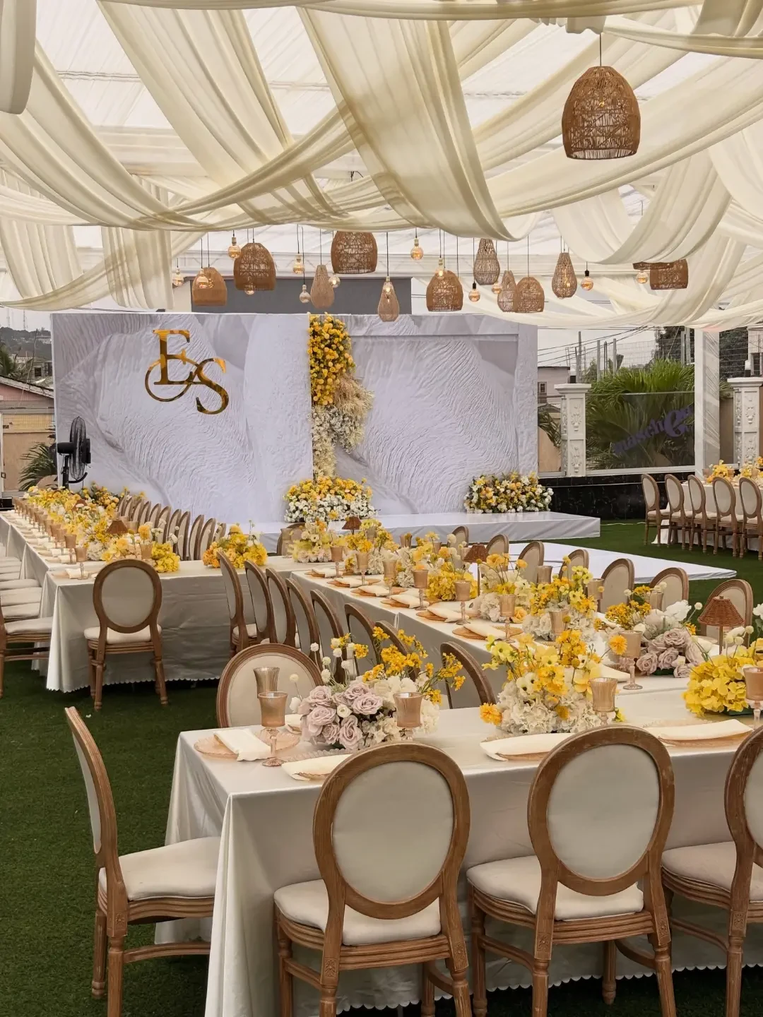 Yellow and cream event with gold monogram backdrop and rattan pendants by Smartest Decor